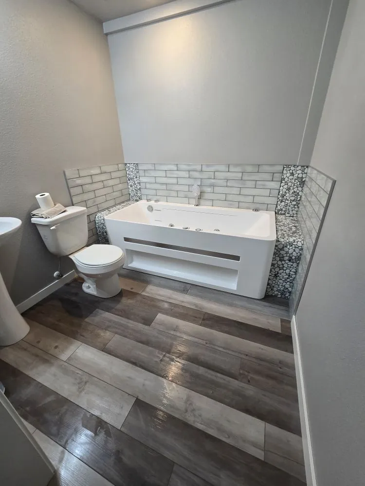 The Jacuzzi Tub Tile Surround · Mandan, ND — custom subway tile with glass-and-pebble accent walls and waterproof LVP flooring.