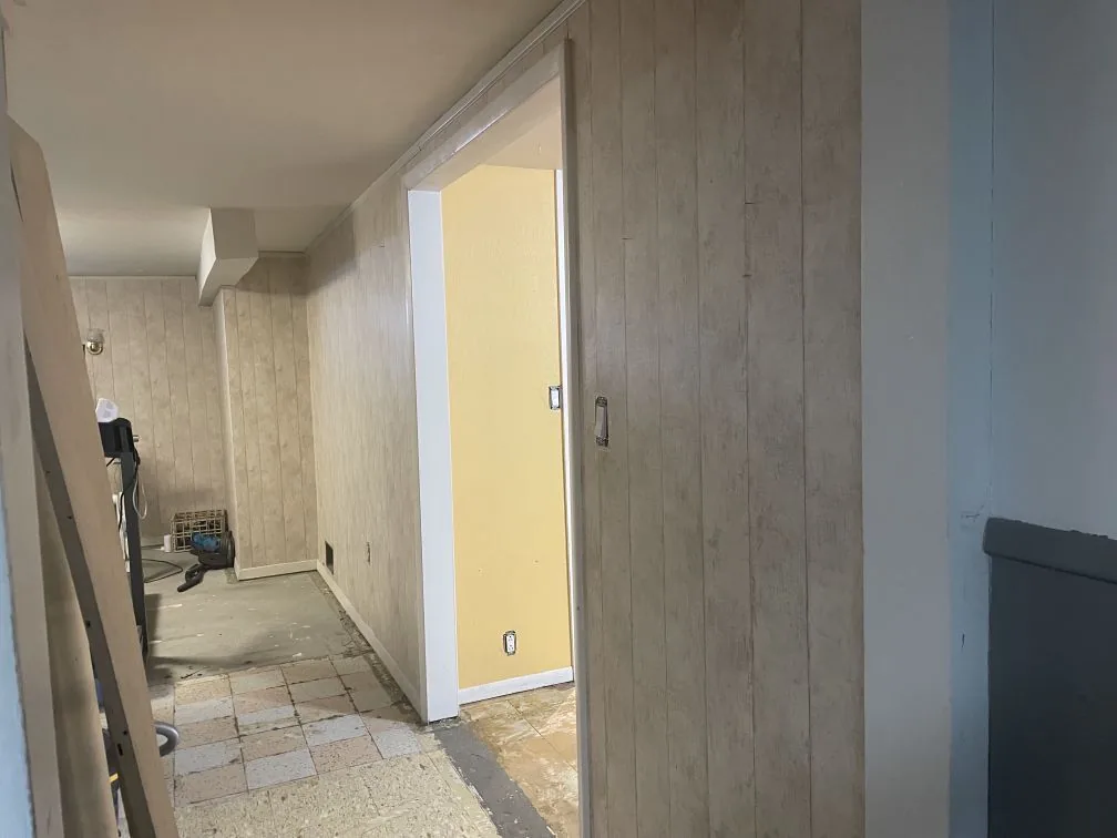 Load-Bearing Wall Removal · Bismarck, ND — before photo of the dated paneled hallway leading into the basement room.
