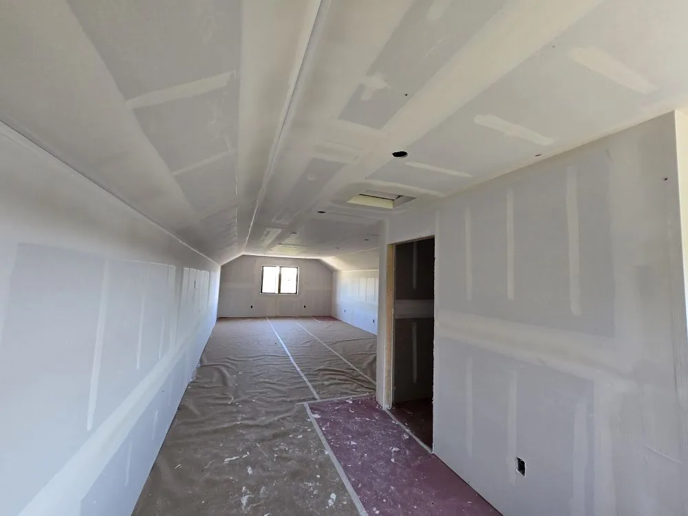 The Ranch Remodel — vaulted bonus room with natural light from the gable-end window during the drywall stage.