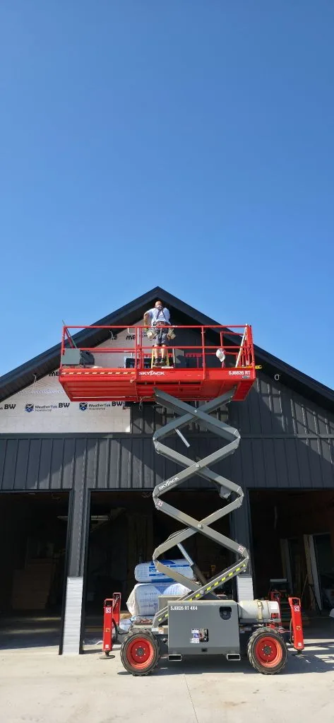 Mid-install on the gable end of the Ranch Remodel — steel siding going up over WeatherTek house wrap from a Skyjack scissor lift.