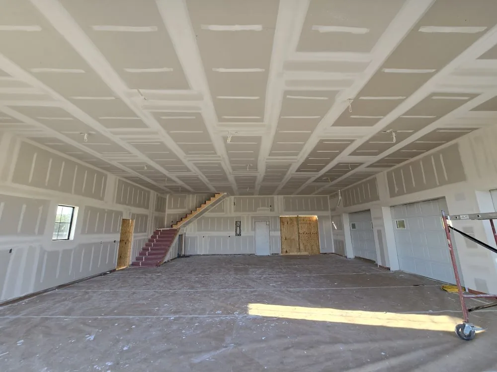 36×42 shop interior at the drywall stage — vaulted ceiling taped, stairs to the bonus room, garage doors set.